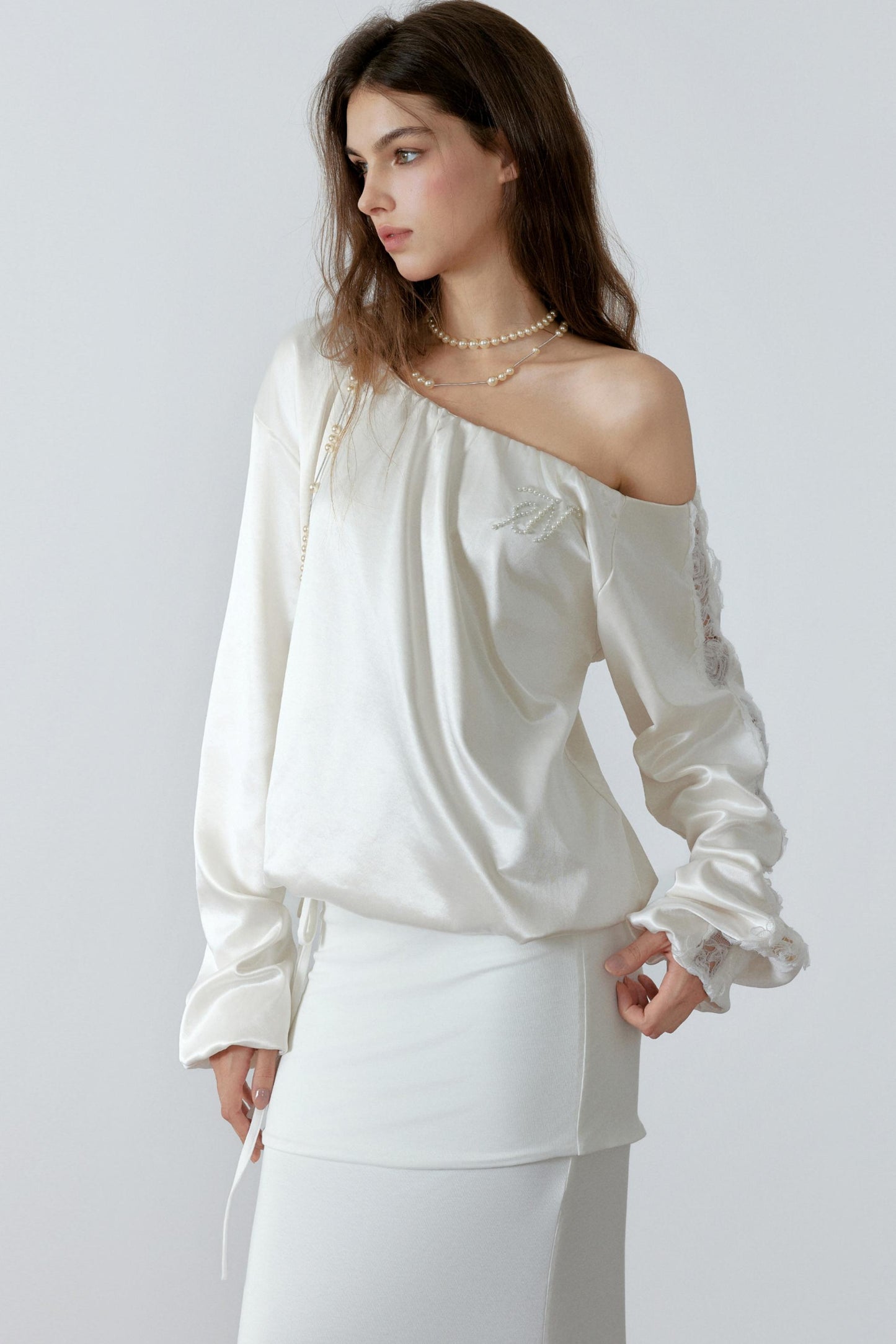 Woman wearing a white off-shoulder top and white pants against a light gray background