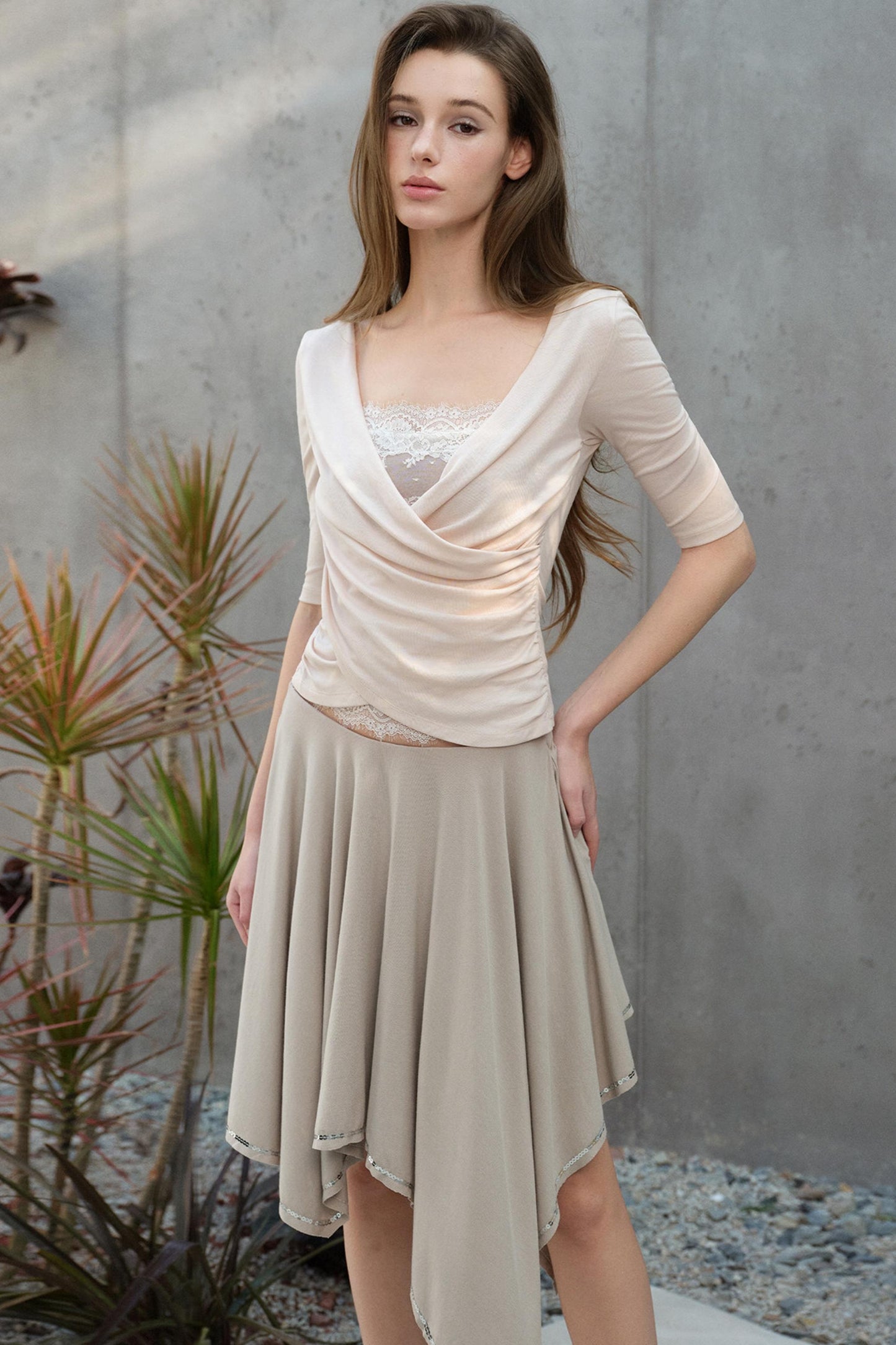 Woman wearing a beige dress standing outdoors with plants in the background