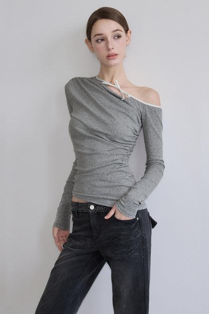 Woman wearing a gray off-shoulder top and black pants against a white background