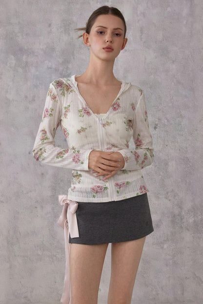 Model wearing a slim-fit floral print pointelle knit hooded cardigan with ribbon details, paired with a dark mini skirt.