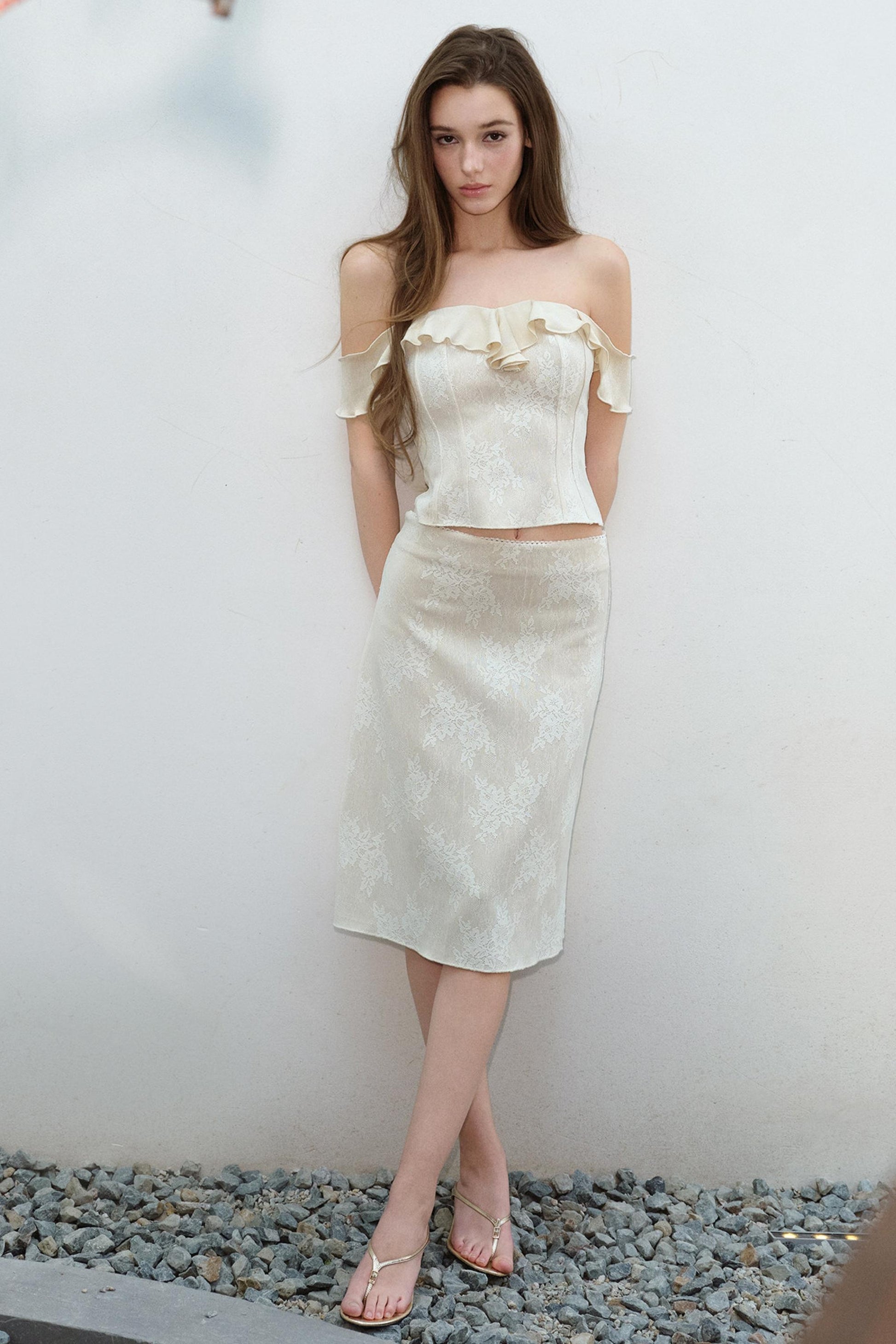 Woman wearing a white off-shoulder top and skirt standing against a plain background.