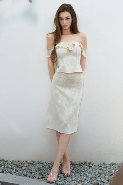 Woman wearing a white off-shoulder top and skirt standing against a plain background.
