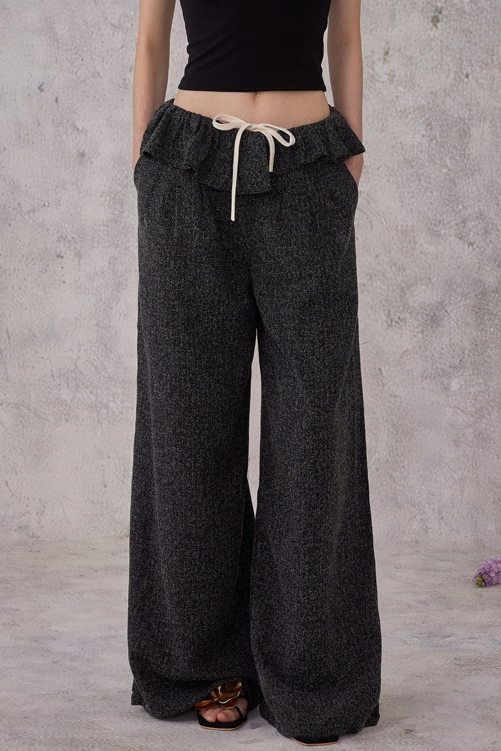 Person wearing dark gray wide-leg pants with a plain background