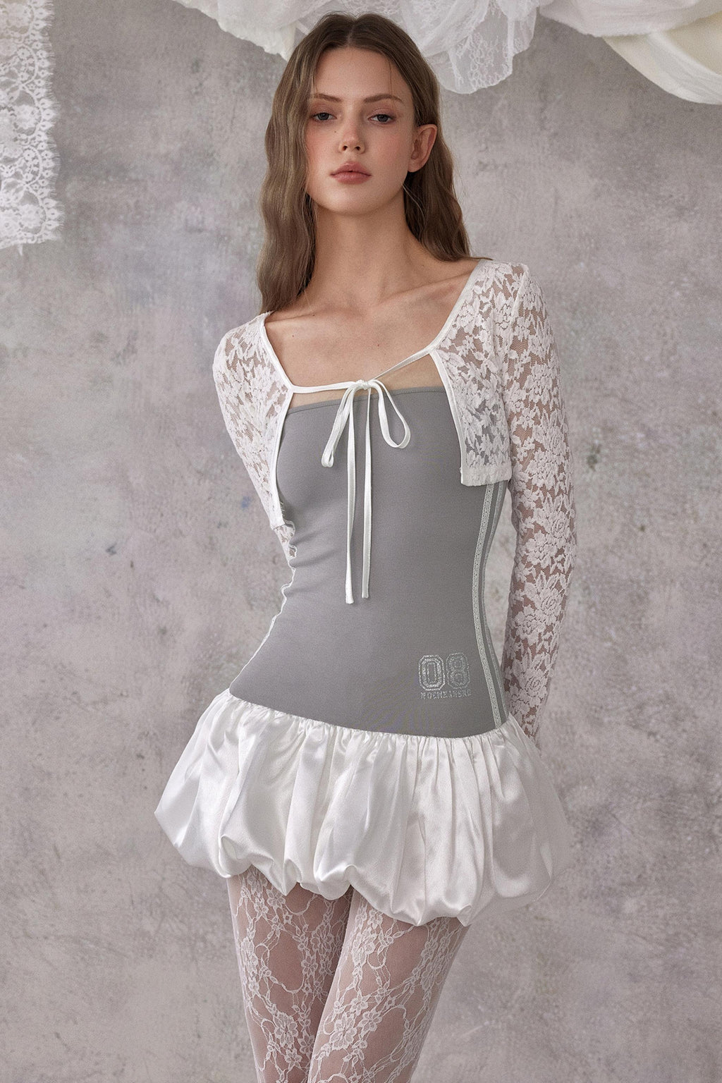 Woman wearing a gray corset with white lace sleeves and skirt against a textured gray background