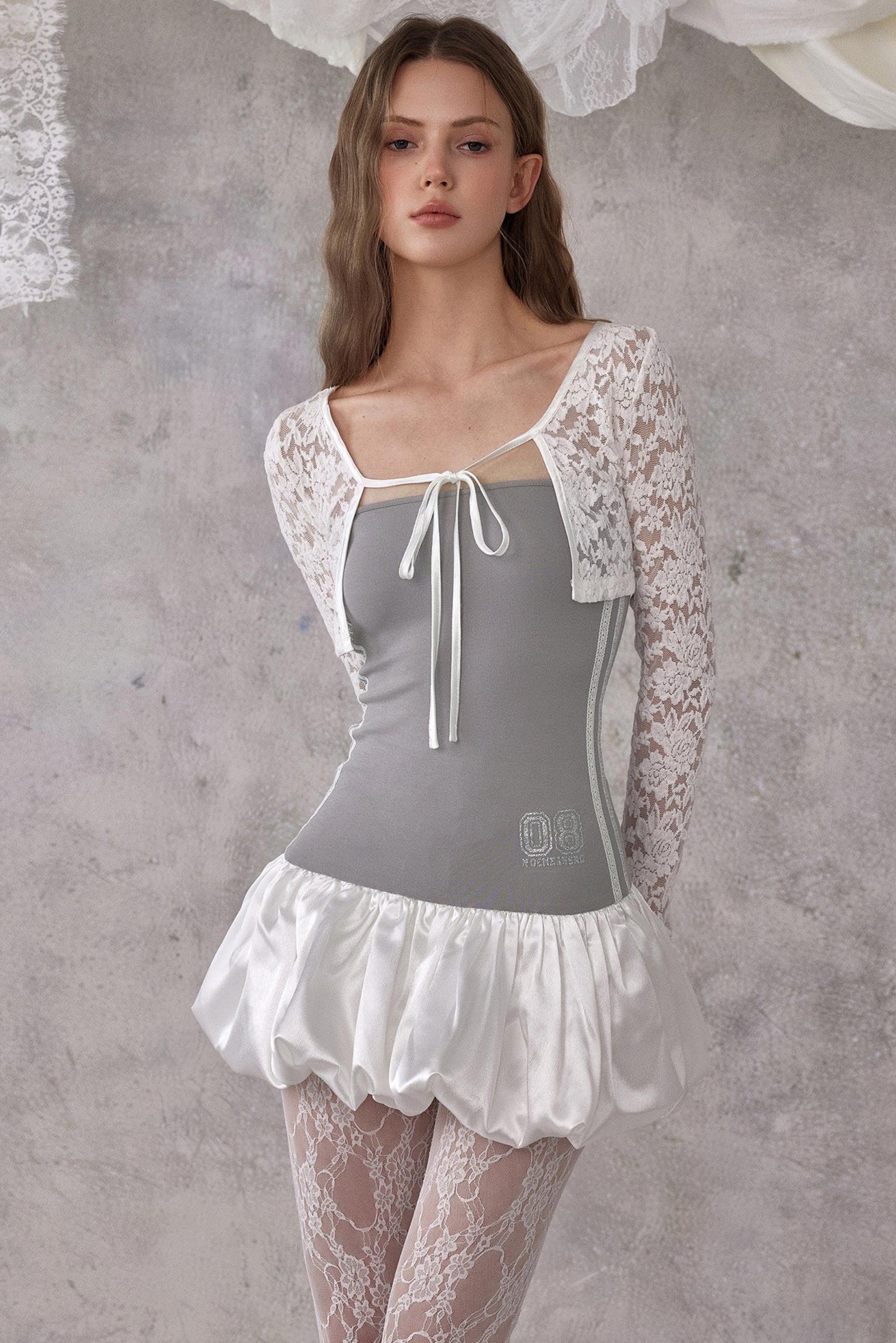 Woman wearing a gray corset with white lace sleeves and skirt against a textured gray background