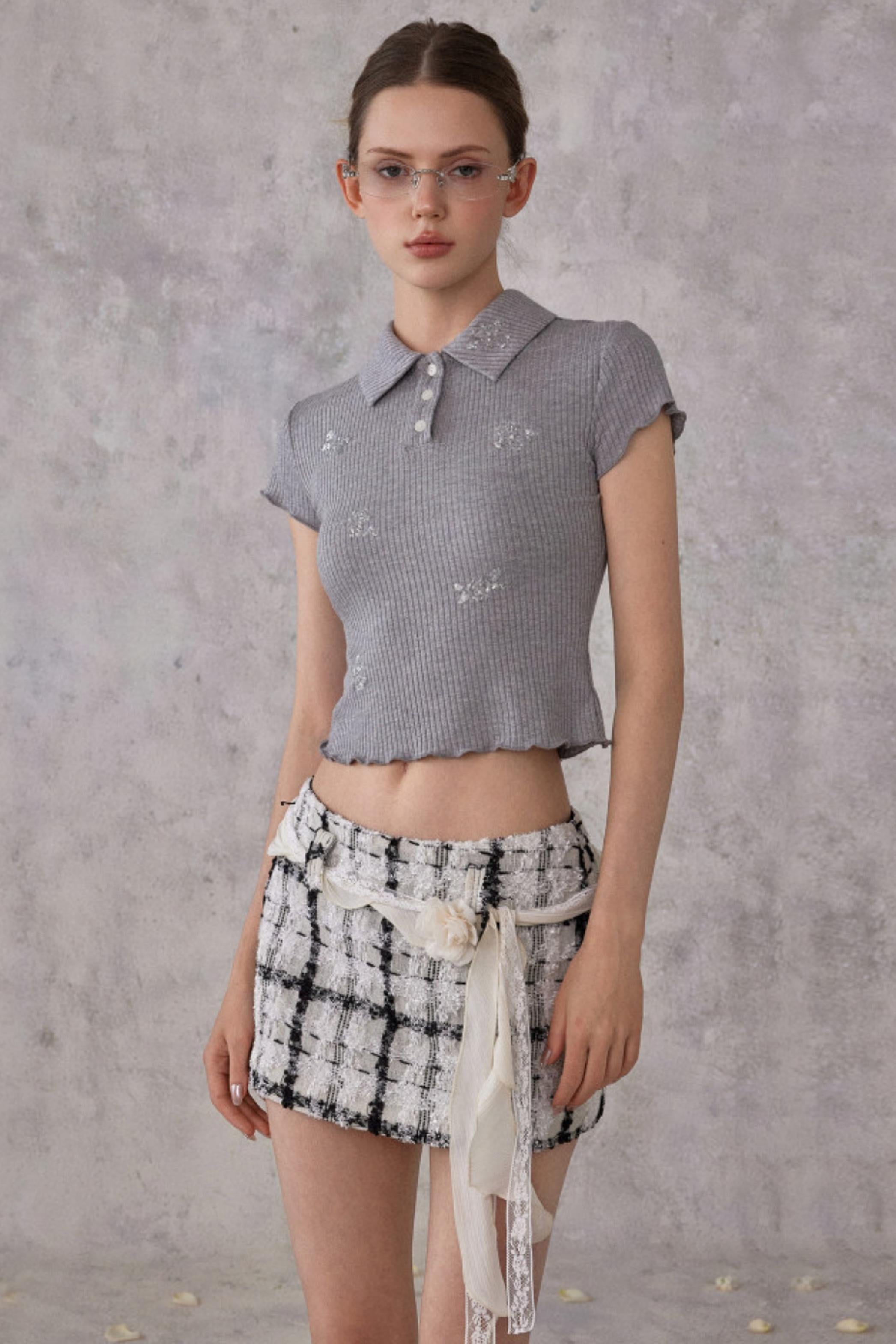 Woman wearing a patterned top and checkered skirt against a gray background