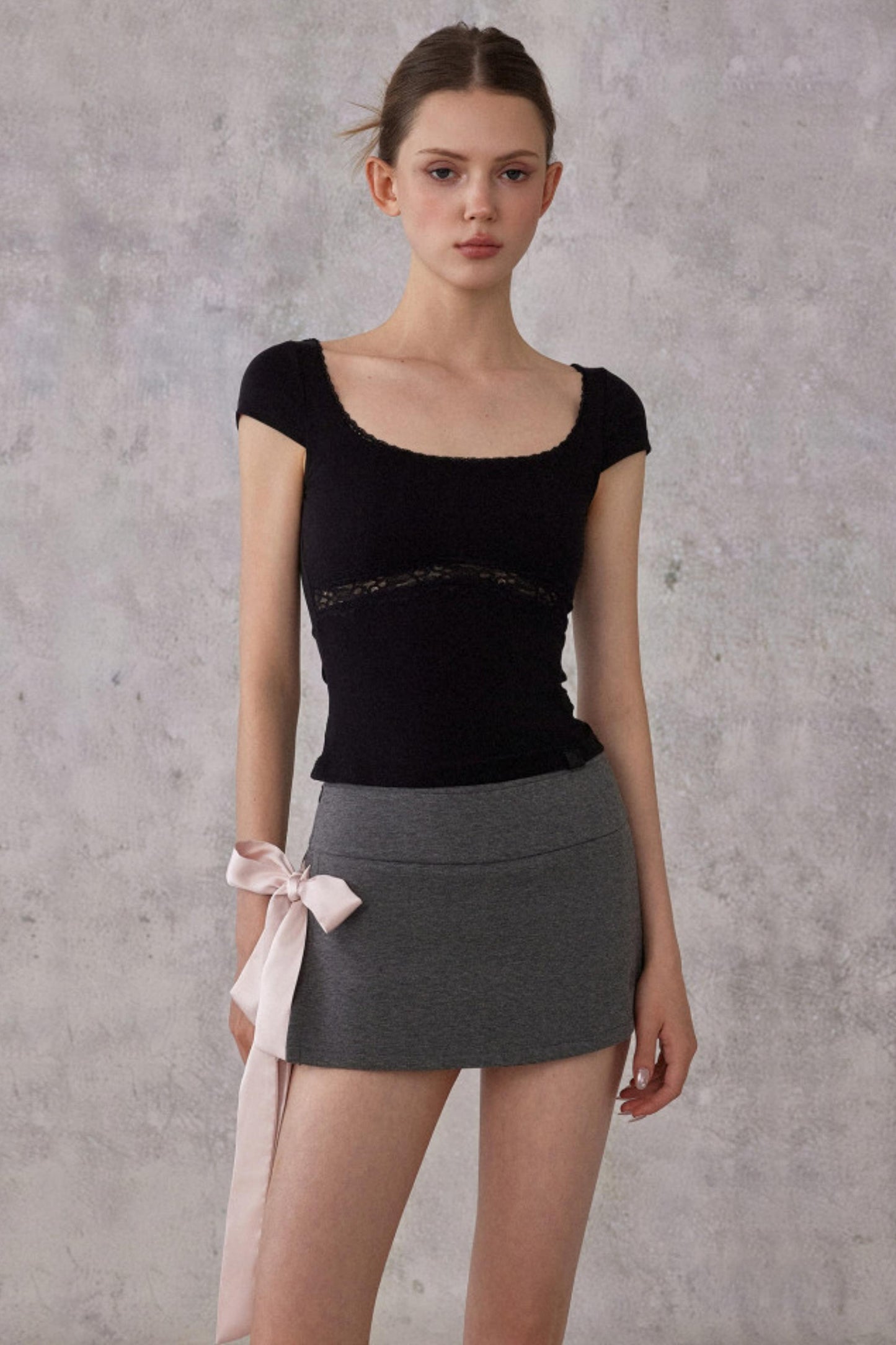 Woman wearing a black top and gray skirt against a plain background
