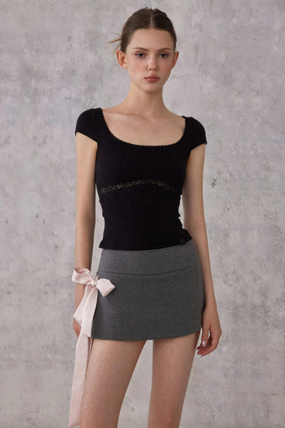 Woman wearing a black top and gray skirt against a plain background