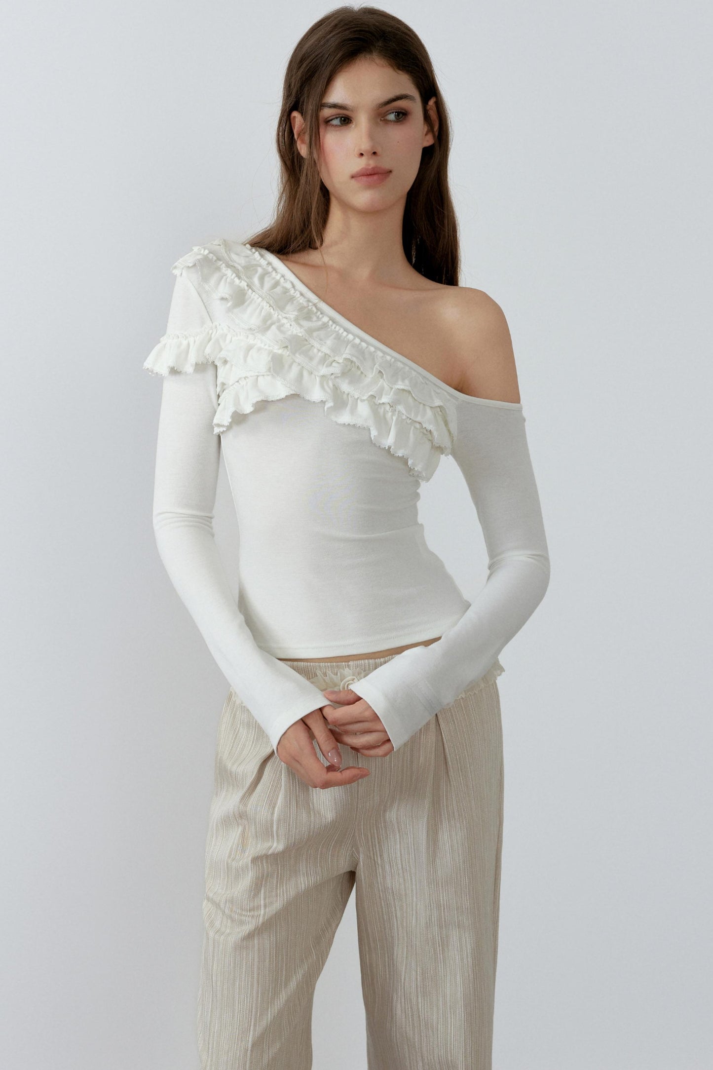 Woman wearing a white one-shoulder top with ruffle details on a plain background