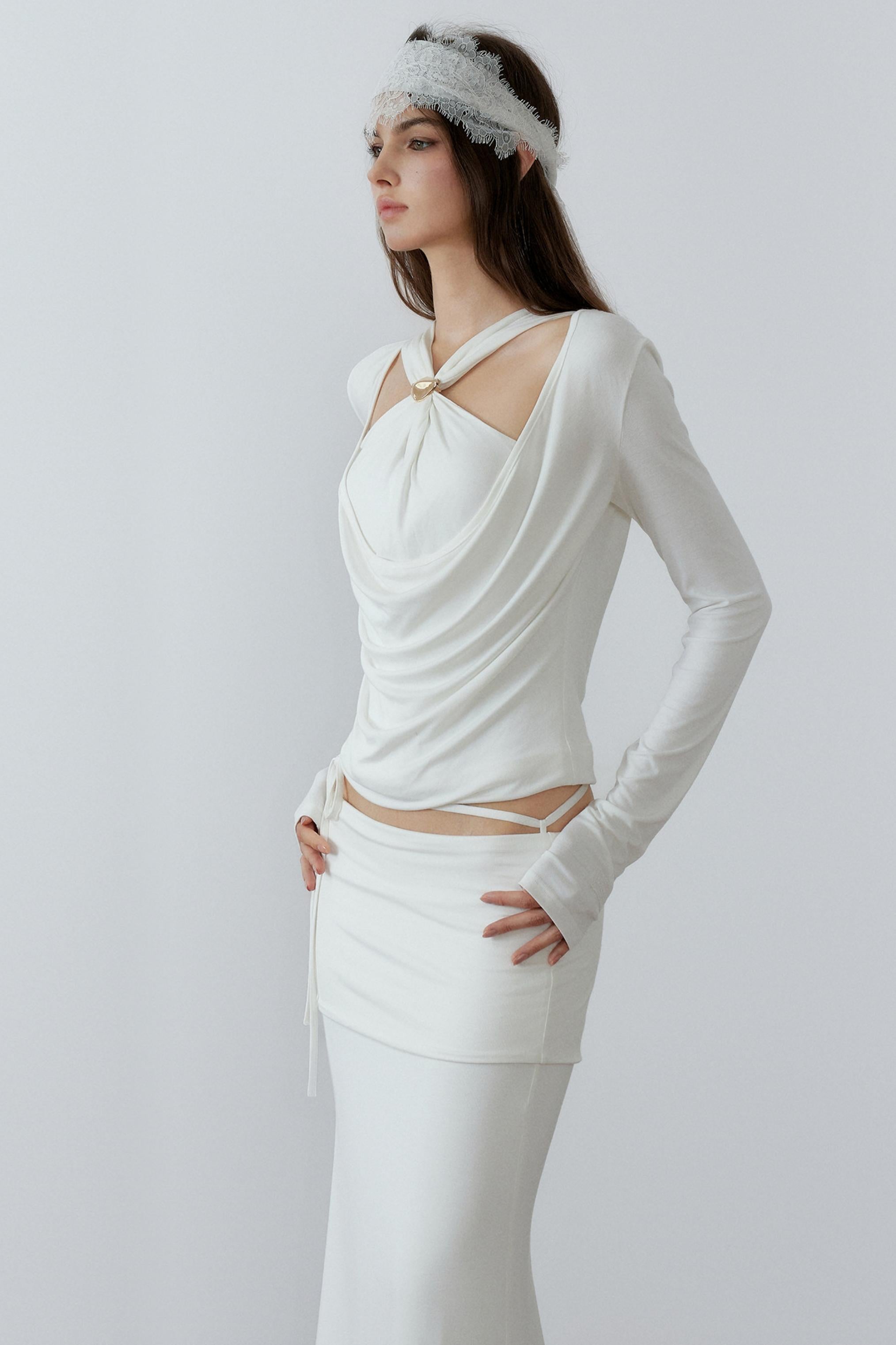 Model showcasing a chic cream long sleeve fake two-piece top featuring a draped cowl neck, halter straps, and a sleek metal knot detail.