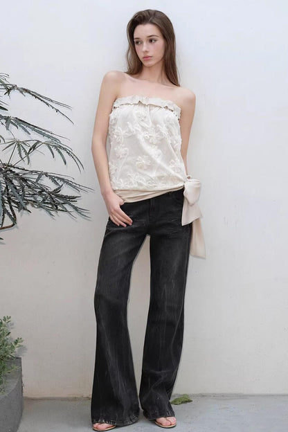 Woman wearing a strapless top and black flared pants against a plain background