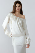 Model posing in an elegant cream off-the-shoulder satin sweatshirt with a relaxed silhouette and three-dimensional lace cut-out details along the sleeves.