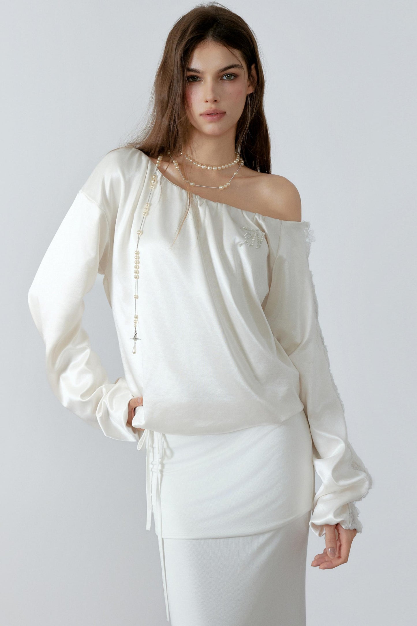 Model posing in an elegant cream off-the-shoulder satin sweatshirt with a relaxed silhouette and three-dimensional lace cut-out details along the sleeves.