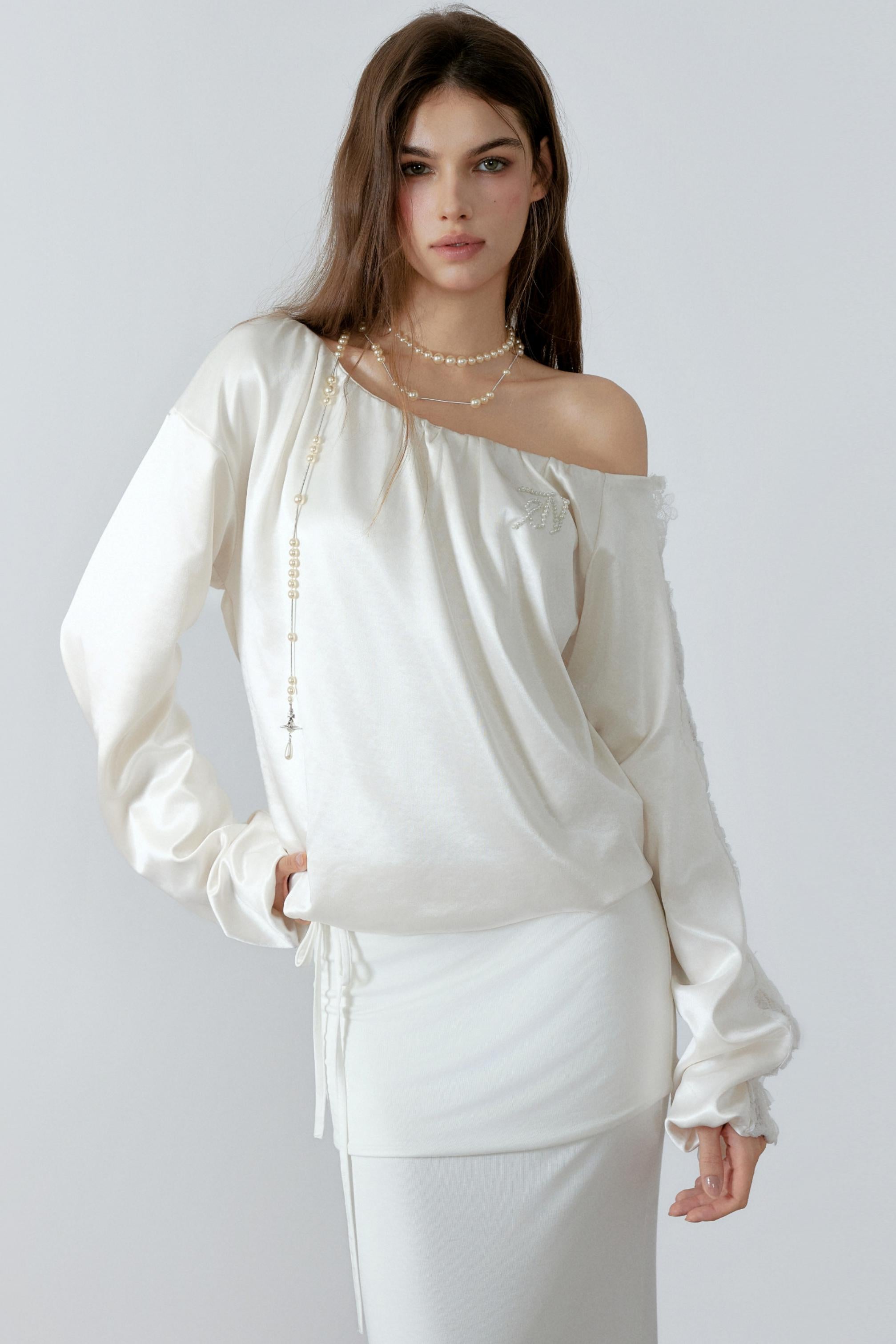 Model posing in an elegant cream off-the-shoulder satin sweatshirt with a relaxed silhouette and three-dimensional lace cut-out details along the sleeves.