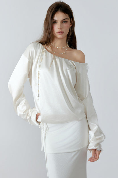 Model posing in an elegant cream off-the-shoulder satin sweatshirt with a relaxed silhouette and three-dimensional lace cut-out details along the sleeves.