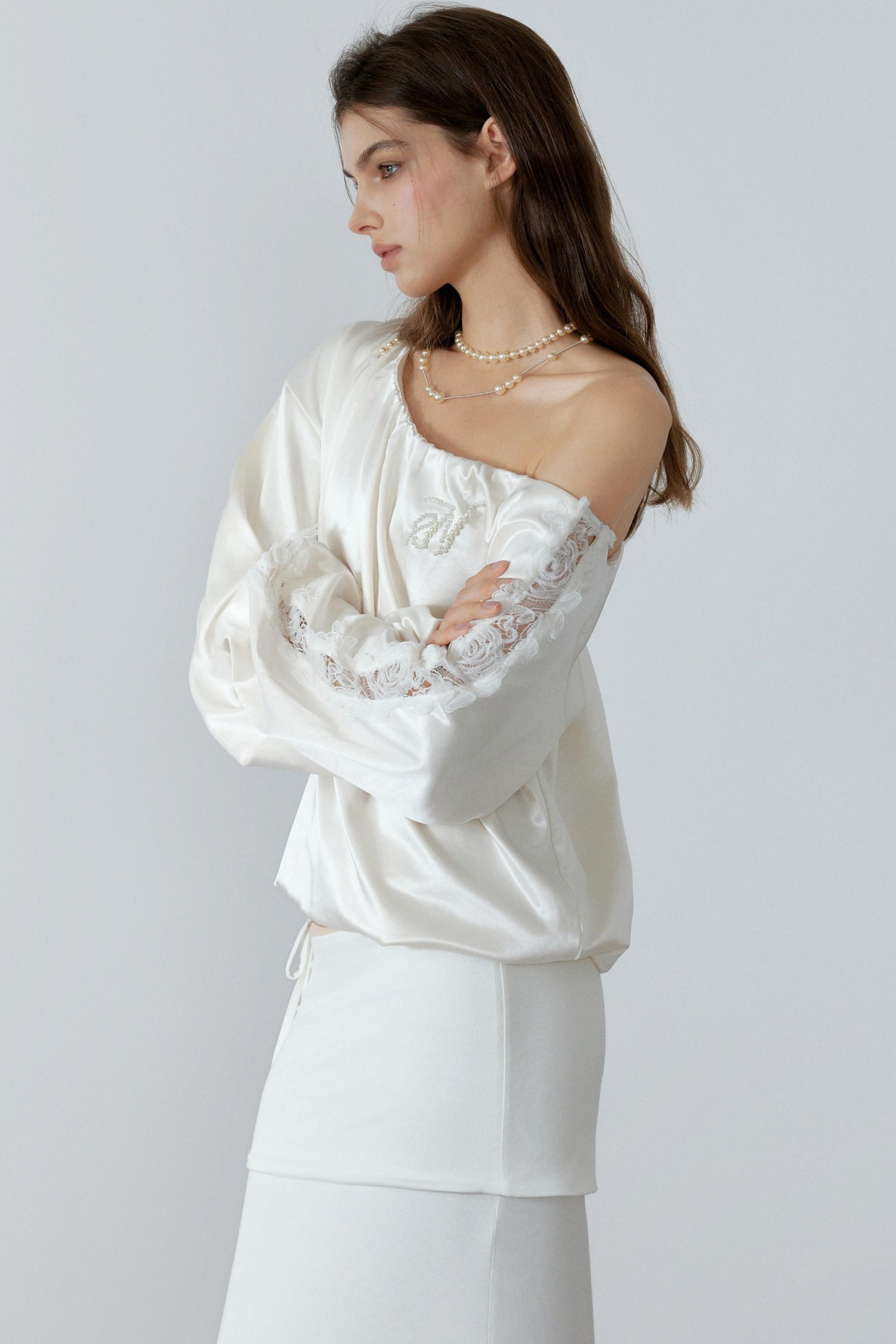 Woman wearing a white off-shoulder top with lace sleeves on a plain background