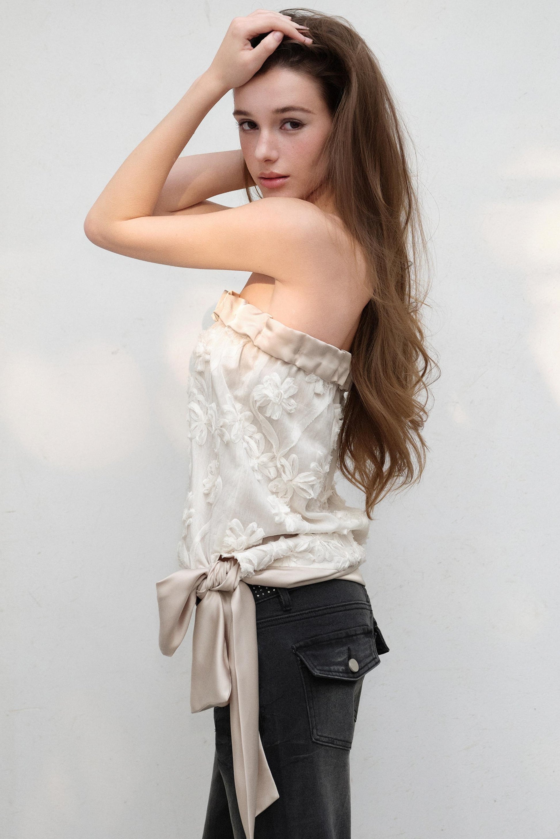 Woman wearing a strapless top with floral patterns and tied fabric, standing against a plain background.