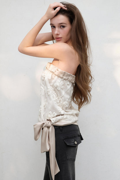 Woman wearing a strapless top with floral patterns and tied fabric, standing against a plain background.