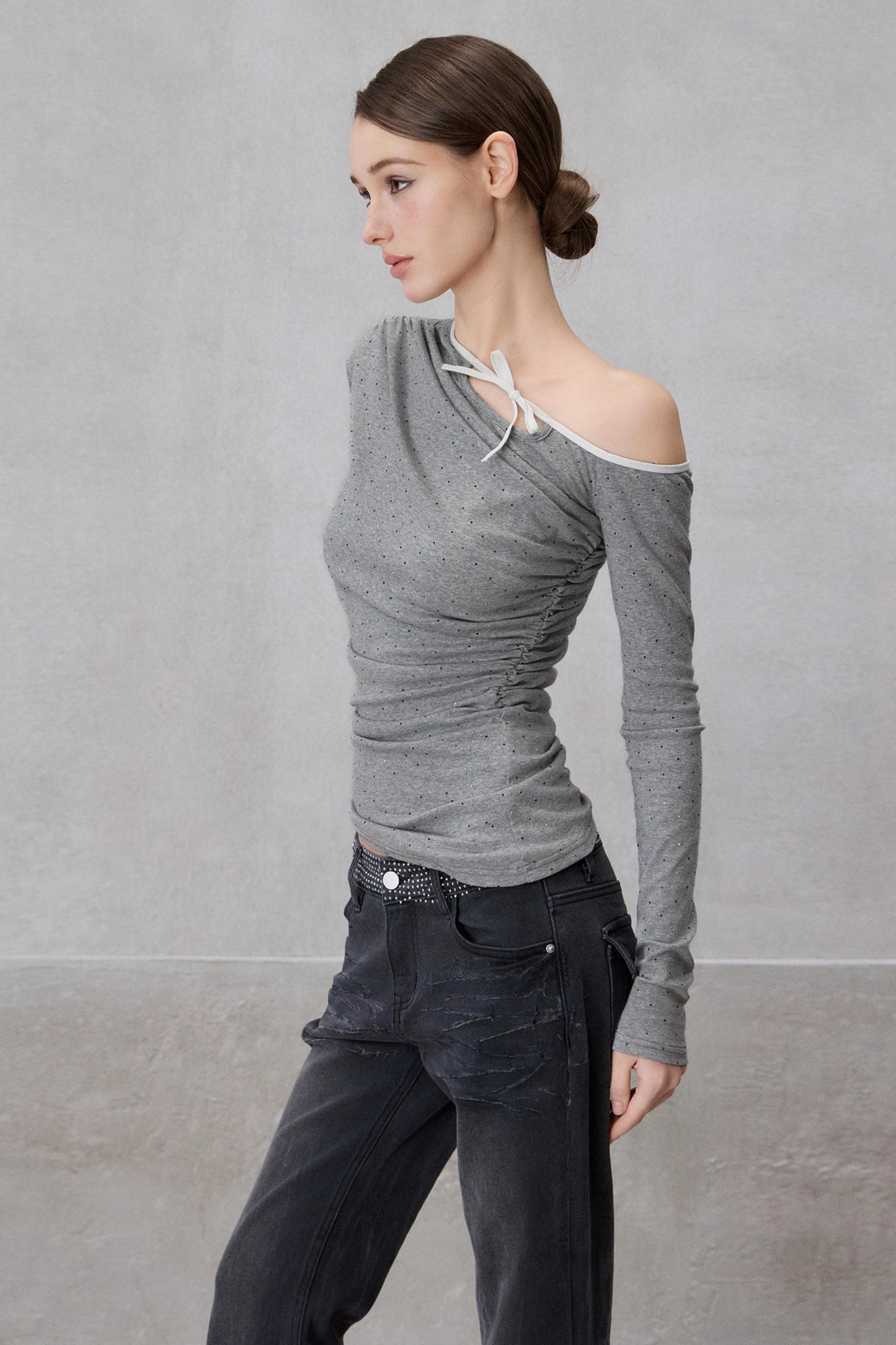 Woman wearing a gray off-shoulder top and dark pants against a plain background