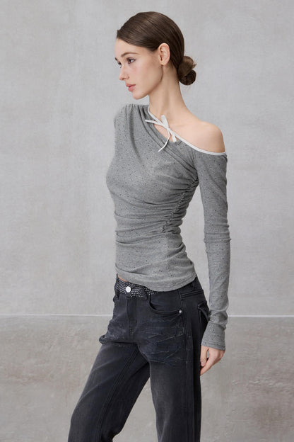 Woman wearing a gray off-shoulder top and dark pants against a plain background