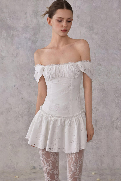 Model styling a romantic white cotton mini dress with eyelet lace details and a smocked pleated waist, worn in a feminine balletcore aesthetic.