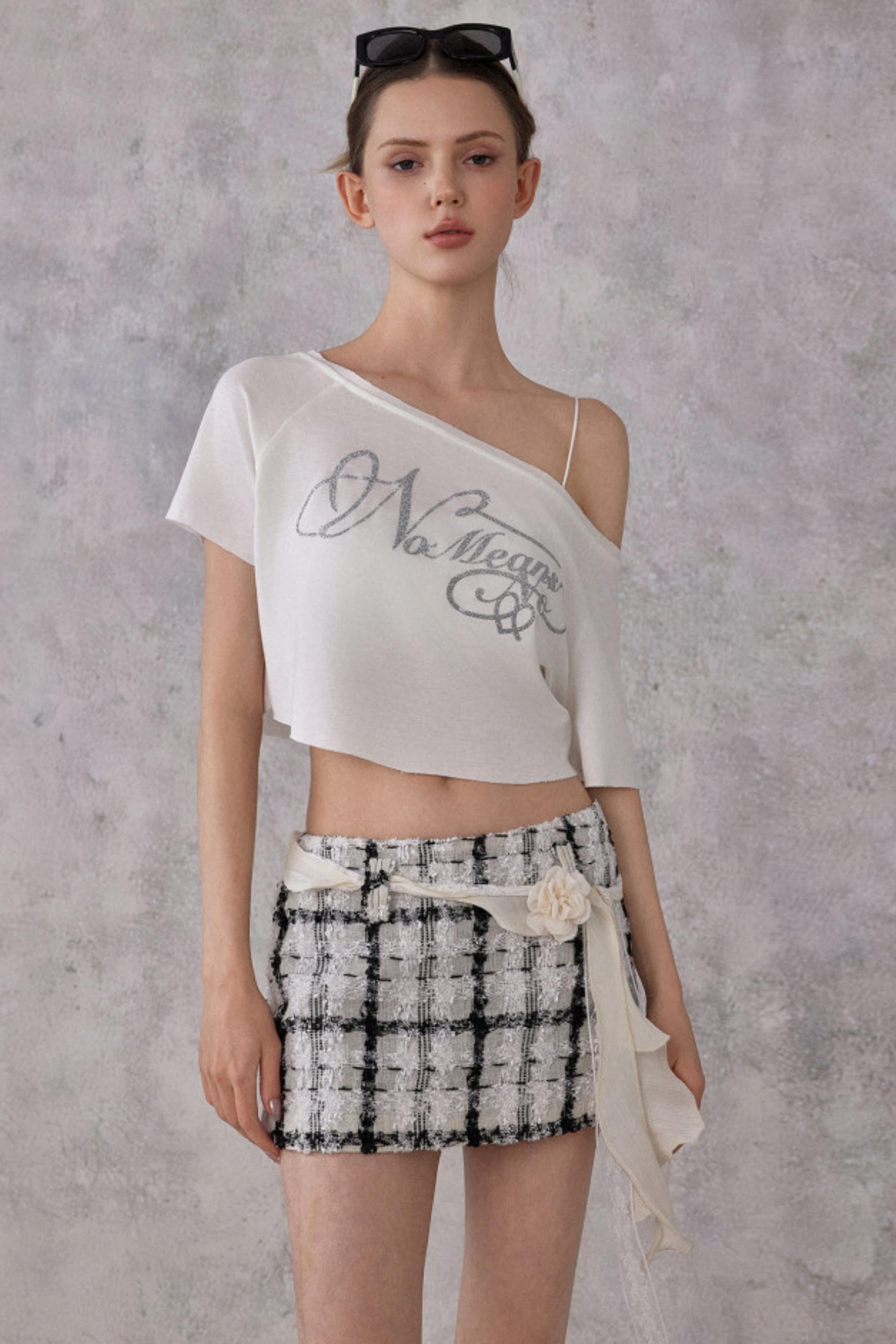 Woman wearing a white one-shoulder top with text and a patterned skirt against a gray background