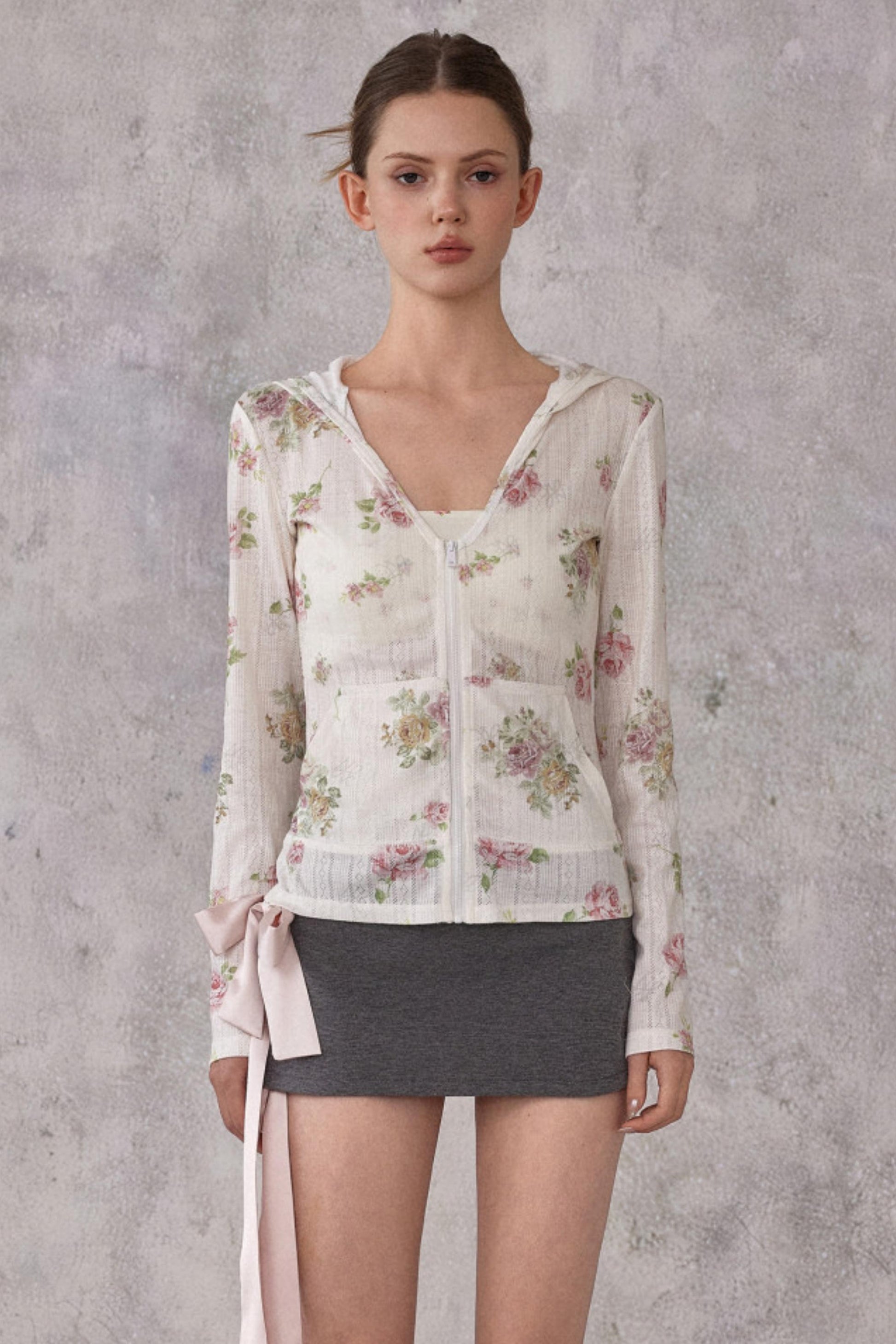 Model wearing a slim-fit floral print pointelle knit hooded cardigan with ribbon details, paired with a dark mini skirt.