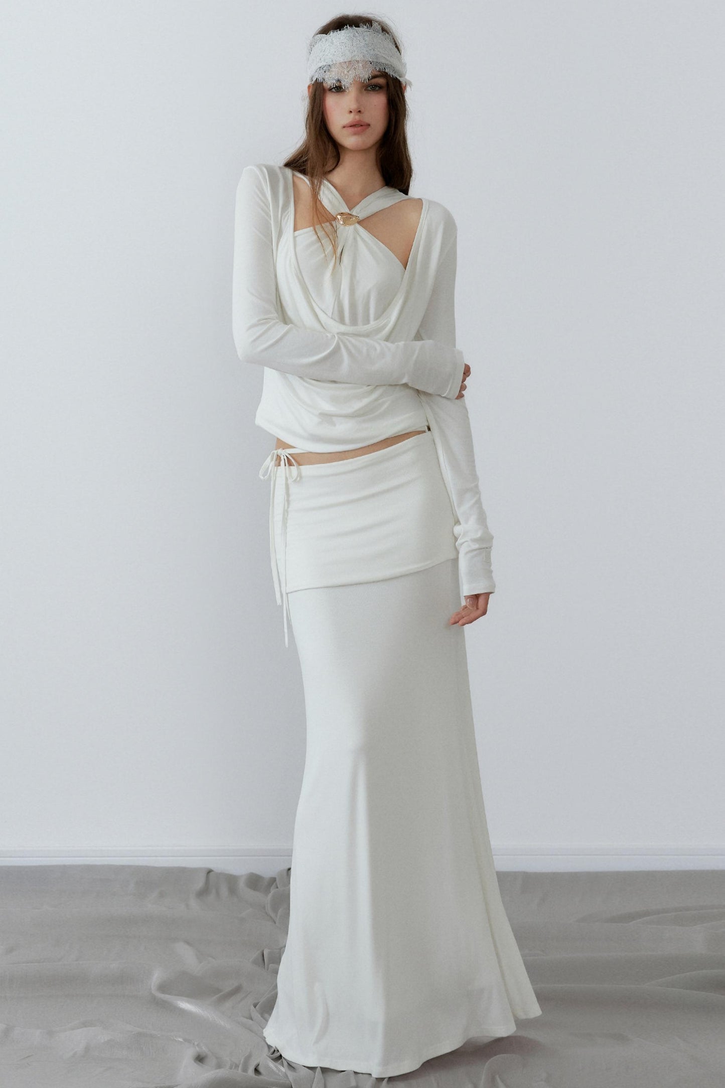 Woman wearing a white dress with long sleeves and a headband against a plain background
