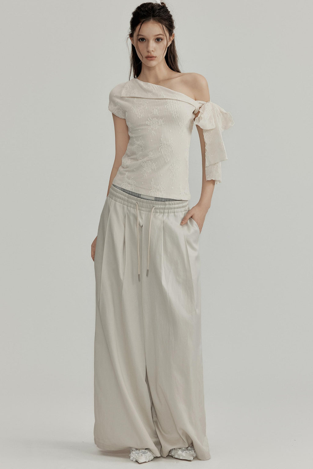 Woman wearing a beige off-shoulder top and flowing pants on a plain background