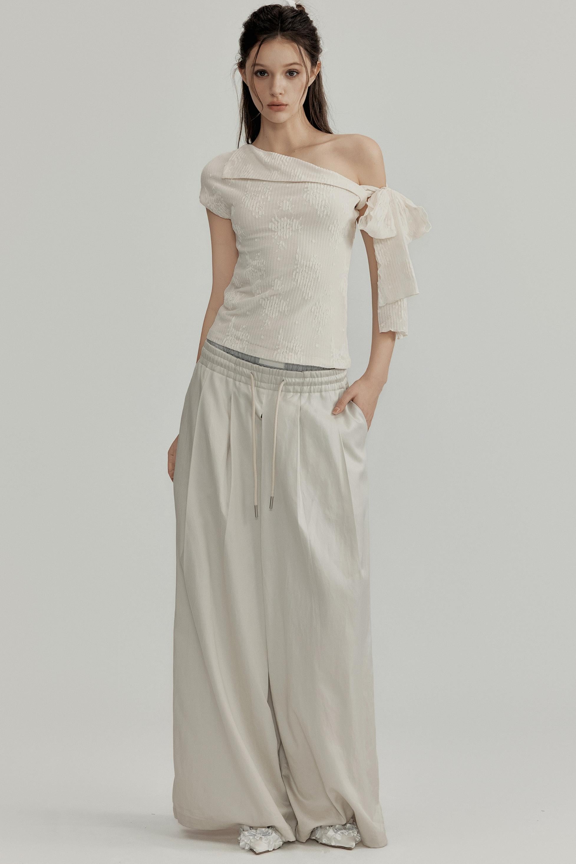 Woman wearing a beige off-shoulder top and flowing pants on a plain background