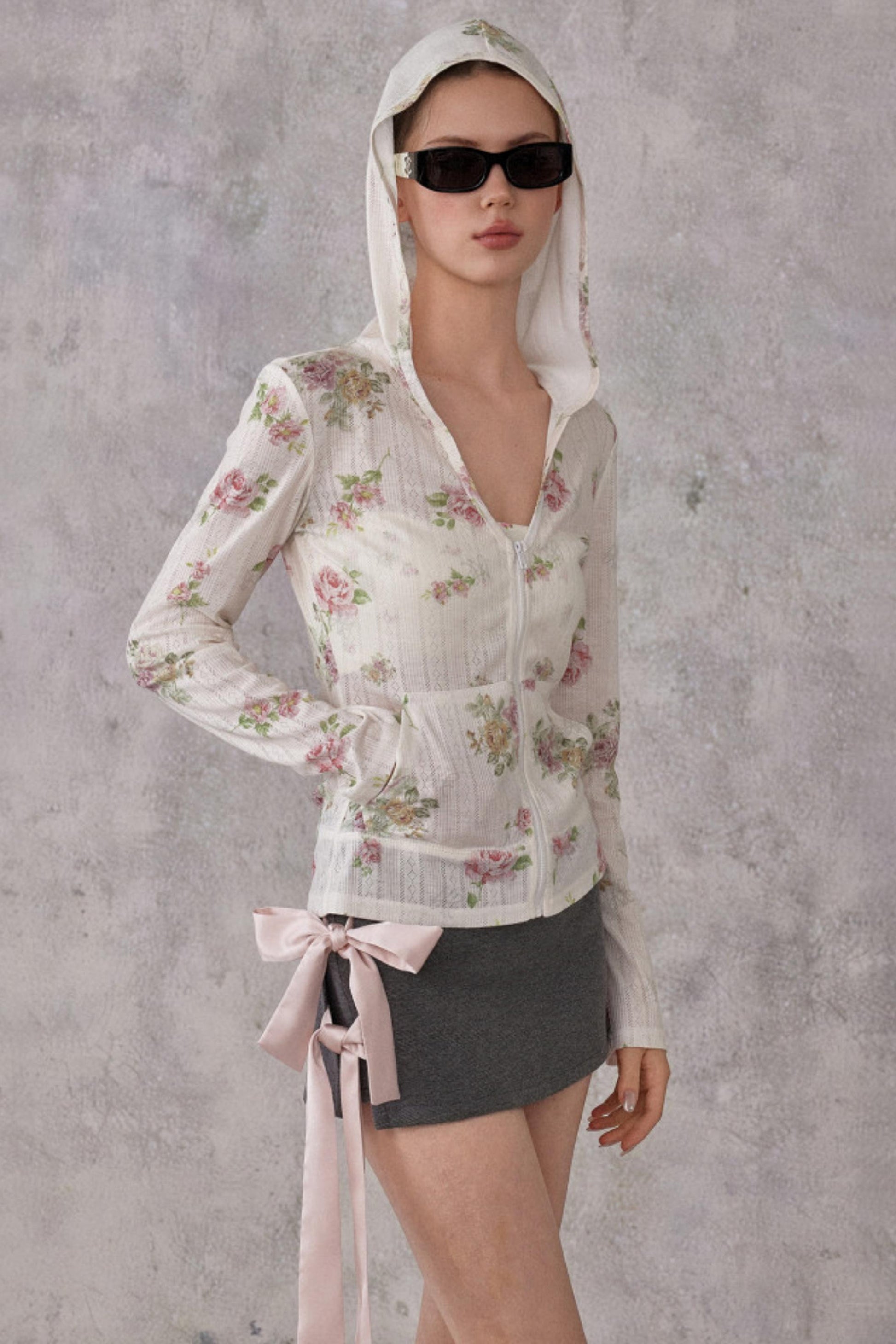 Model wearing a slim-fit floral print pointelle knit hooded cardigan with ribbon details, paired with a dark mini skirt.