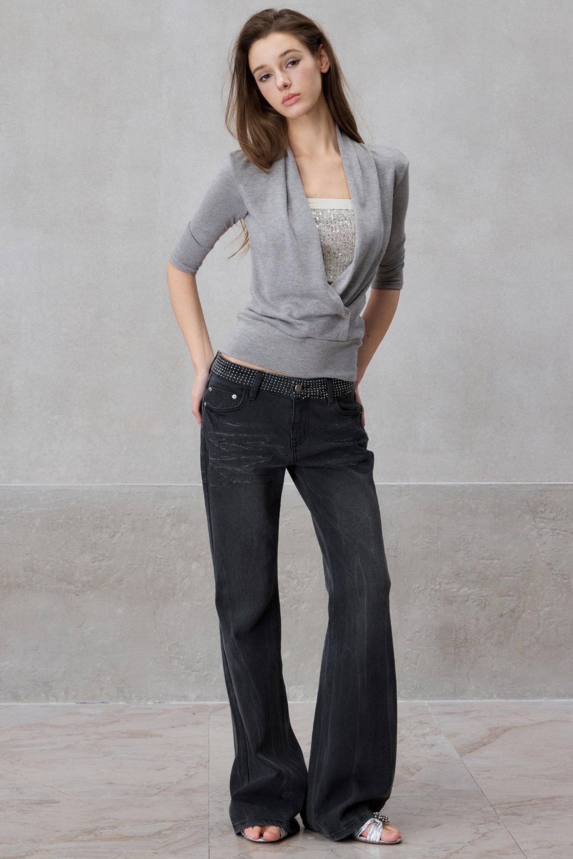 Woman wearing a gray cardigan and black jeans against a plain background