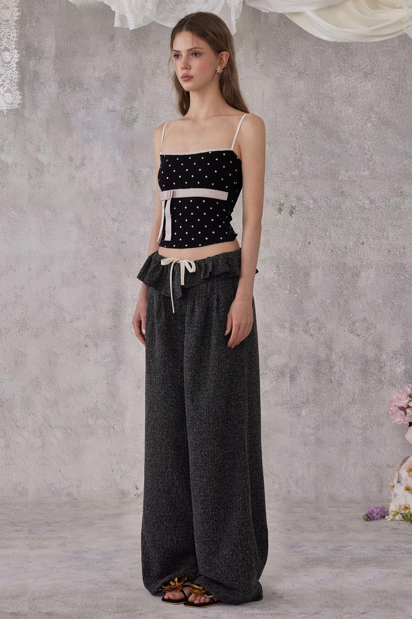 Woman wearing a black polka dot top and dark pants against a gray background