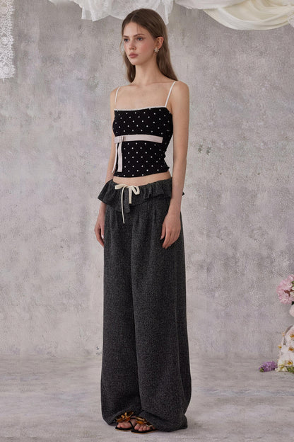 Woman wearing a black polka dot top and dark pants against a gray background