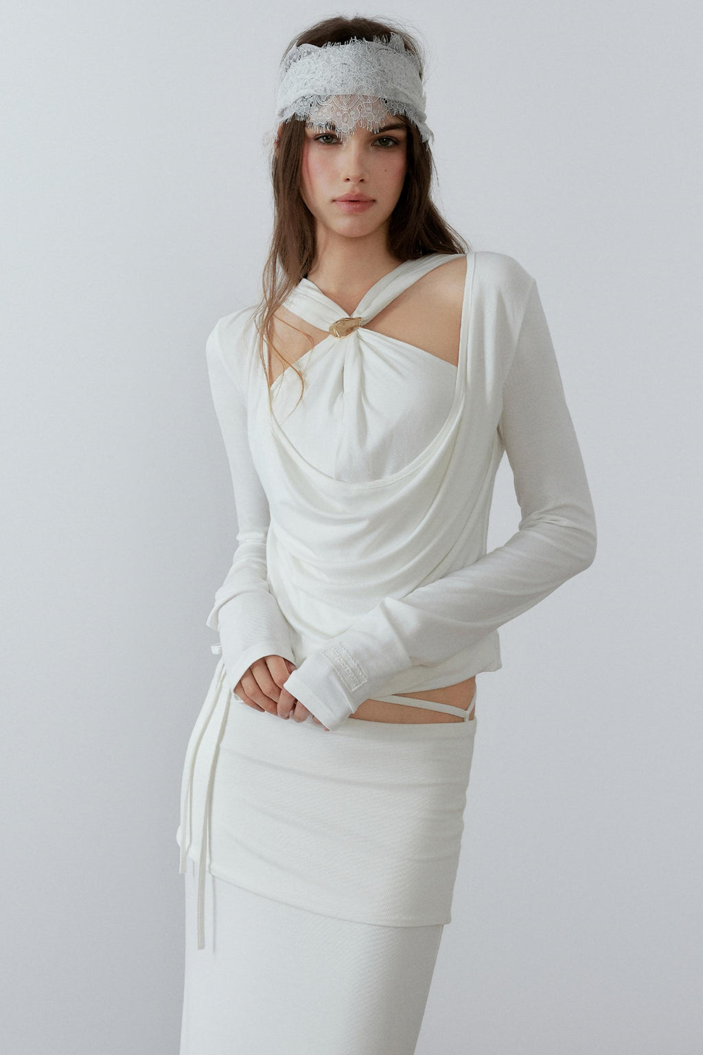 Model showcasing a chic cream long sleeve fake two-piece top featuring a draped cowl neck, halter straps, and a sleek metal knot detail.