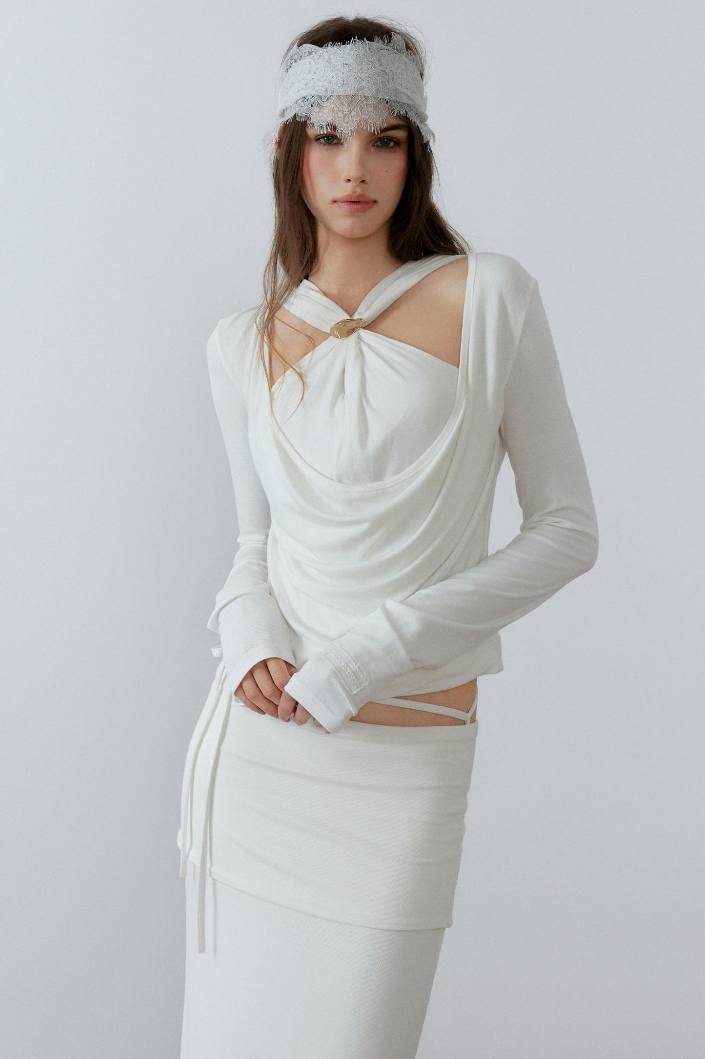 Model showcasing a chic cream long sleeve fake two-piece top featuring a draped cowl neck, halter straps, and a sleek metal knot detail.