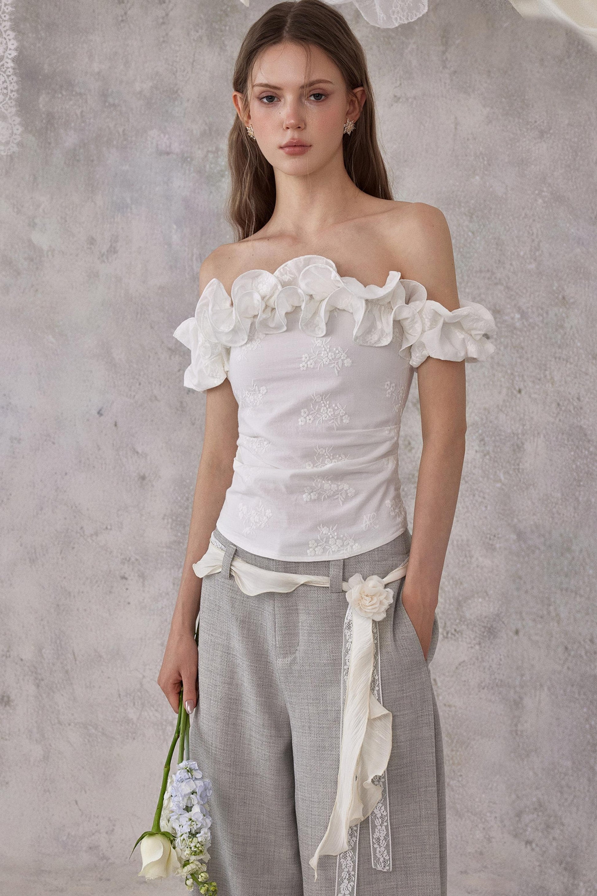 Woman wearing a white off-shoulder top with floral details against a gray background
