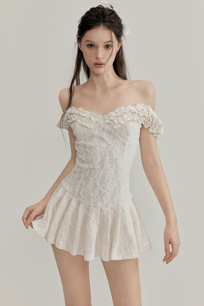 Woman wearing a white lace off-shoulder dress against a plain background