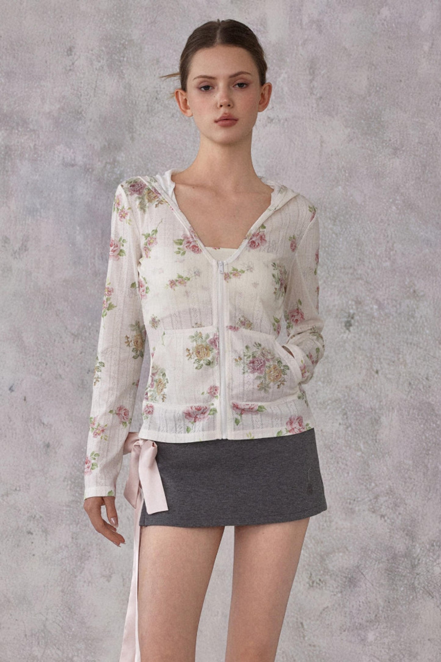 Woman wearing a floral blouse and gray skirt against a textured gray background
