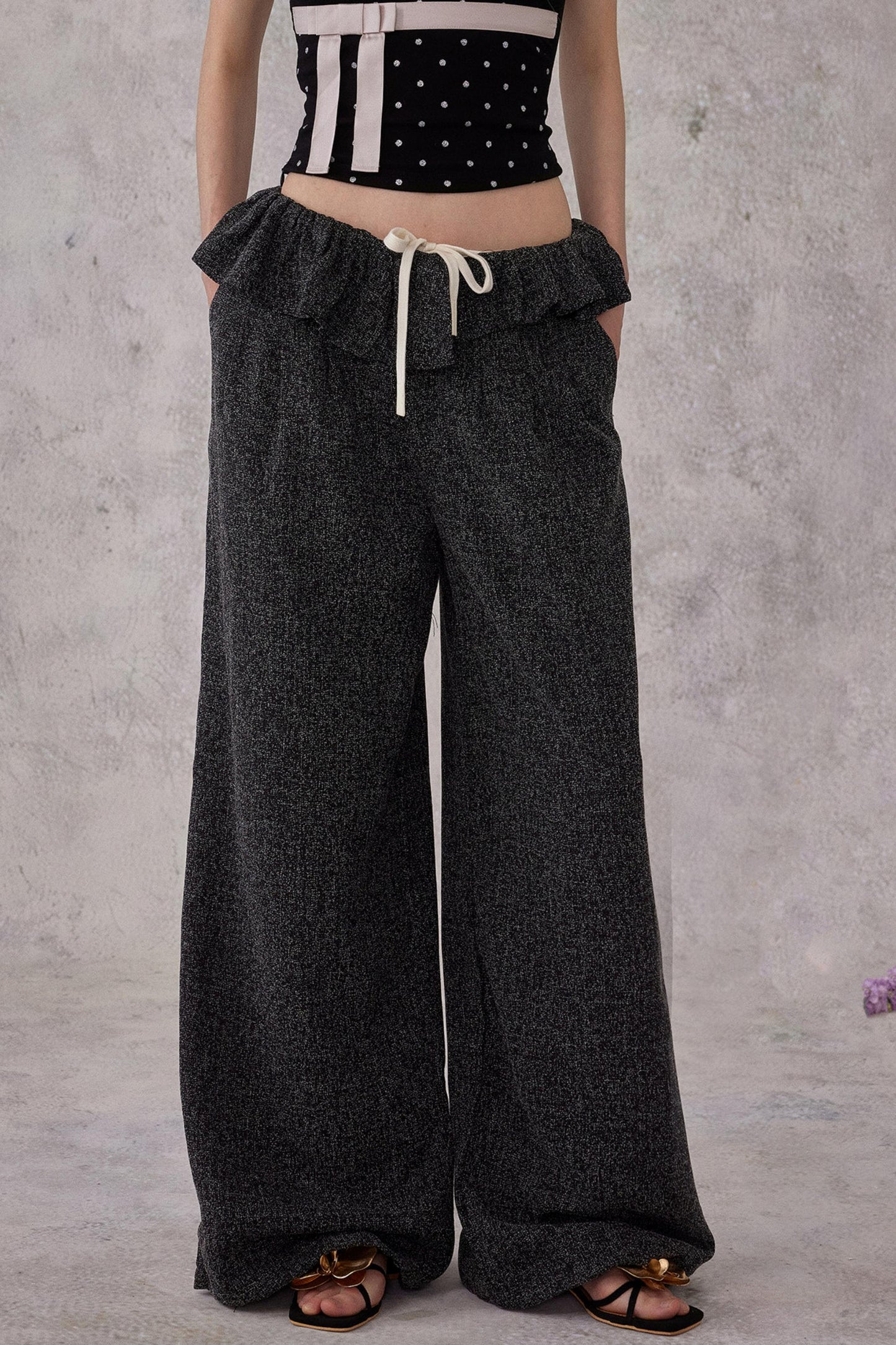Model wearing black ballet ruffled wide-leg trousers with a drawstring waist and a subtle shimmer finish, styled with sandals.