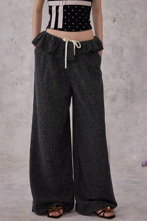 Model wearing black ballet ruffled wide-leg trousers with a drawstring waist and a subtle shimmer finish, styled with sandals.