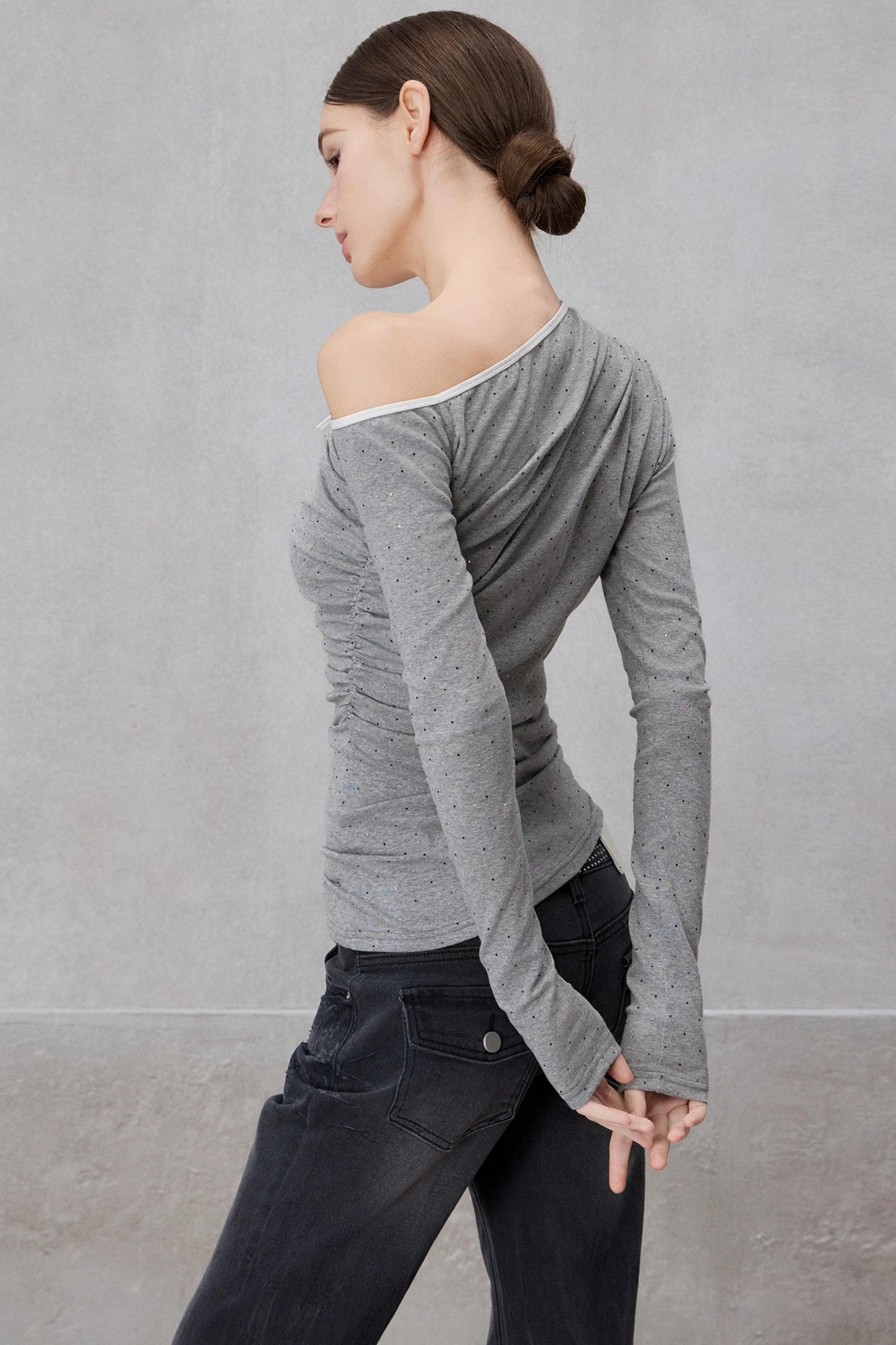 Woman wearing a gray off-shoulder long-sleeve top against a plain background