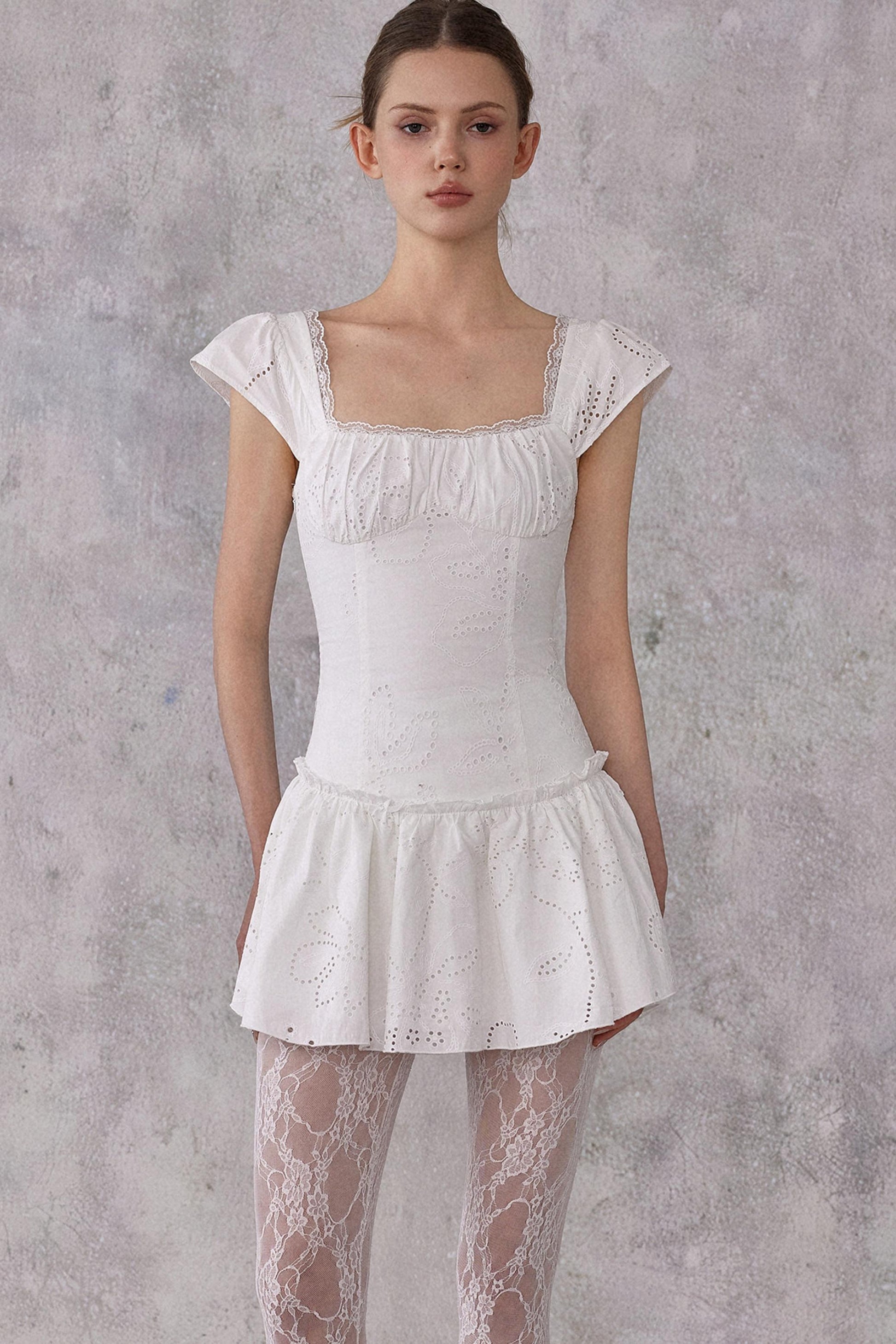 Woman wearing a white lace dress against a gray background