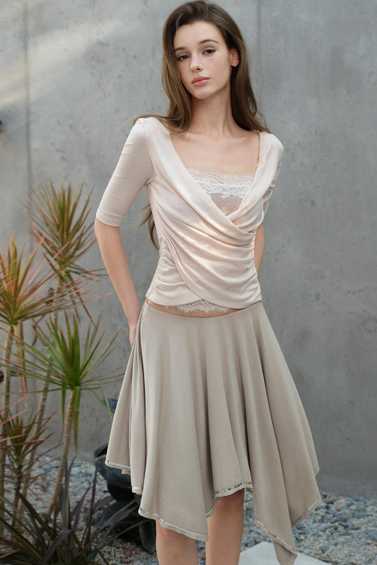 Woman wearing a beige dress with a lace top against a gray wall.