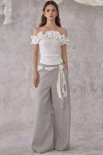 Woman wearing a white floral top and gray wide-leg pants against a textured gray background