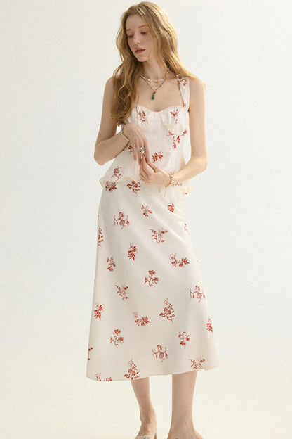 A woman modeling a sleeveless white midi dress with a red floral print and ruffled neckline, photographed against a plain light background.