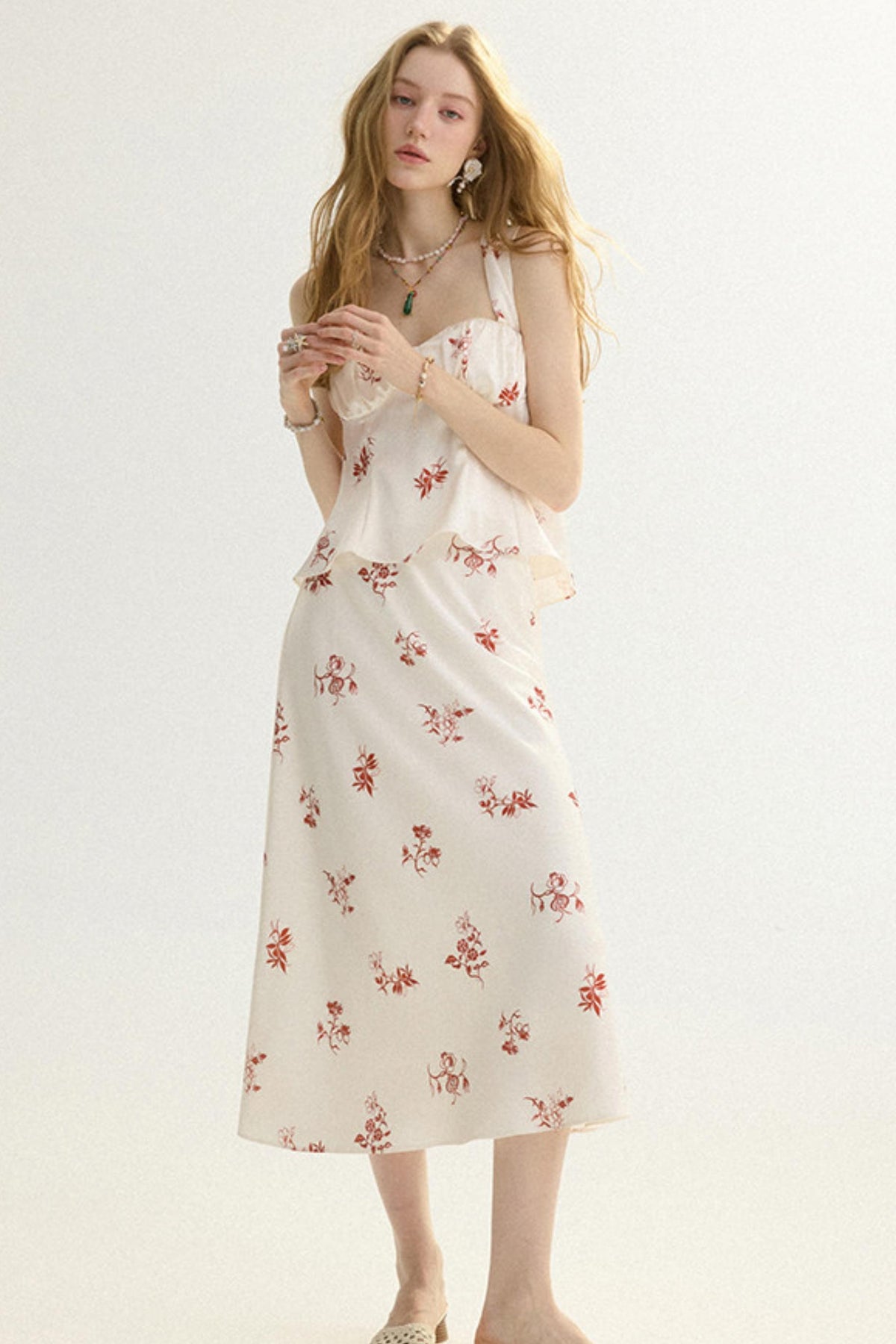 A woman modeling a sleeveless midi dress with a white base and a small red floral print, set against a plain light background.