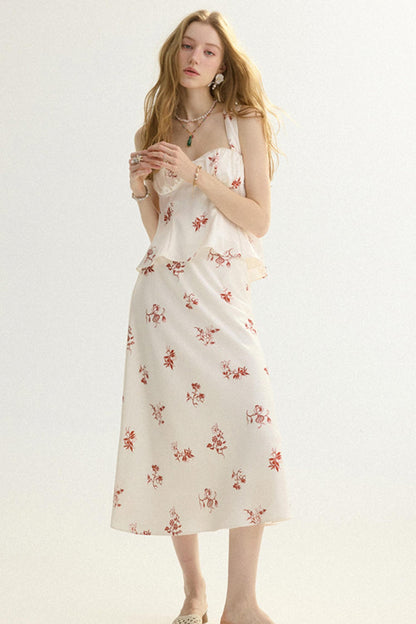 A woman modeling a sleeveless midi dress with a white base and a small red floral print, set against a plain light background.