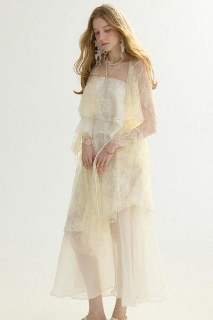 A woman modeling a long cream-colored dress with a sheer lace overlay and ruffled layers, photographed against a plain light background.
