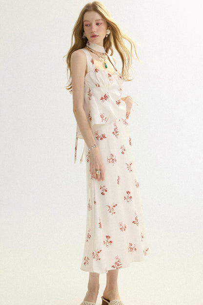 A woman modeling a sleeveless cream midi dress with a red floral print and a matching cropped tie-front overlay, photographed against a plain light background.
